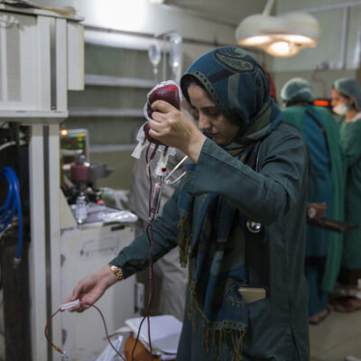 A woman holds a bag of blood in the air, preparing it for a transfusion