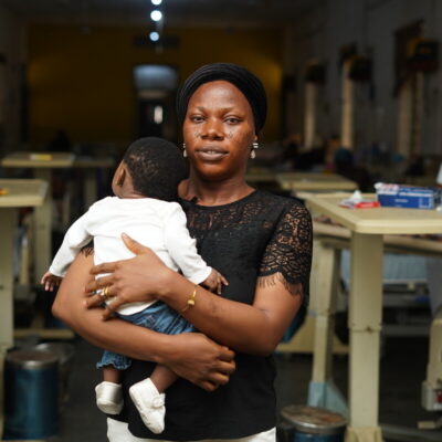 A woman on a maternity ward in Nigeria holds her baby close to her chest and looks at the camera.