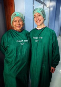 Two women stand in green scrubs and hair nets