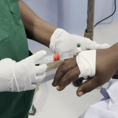 A close-up of a healthcare worker in gloves holding a patient's hand in a medical setting.