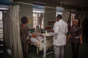 Clinicians stand around a hospital bed talking to a pregnant woman who lies in bed. 