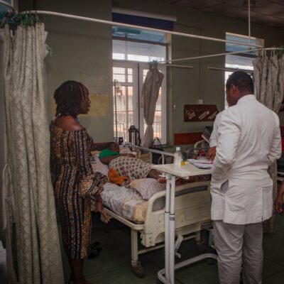 A doctor and a woman standing beside a hospital bed, where a patient is lying down in a clinical setting